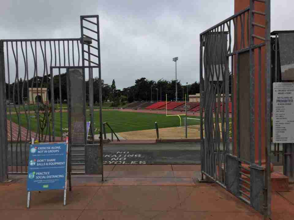 Open entrance gate to Kezar Stadium and track, themselves visible beyond the gates, a warning sign just to the left of the open gate.