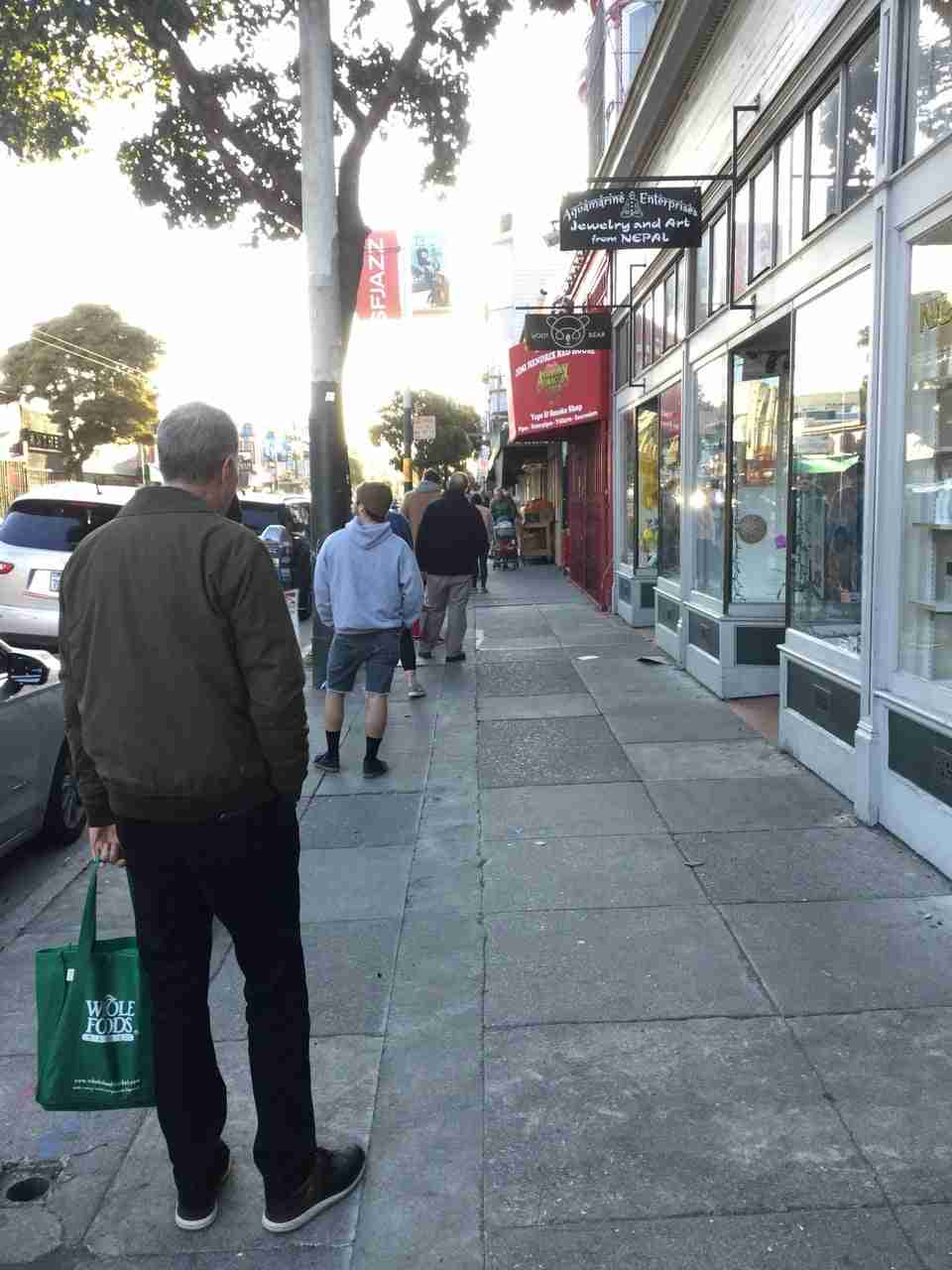 Line of people on the sidewalk on Haight street, about six feet apart, waiting to get into Haight Street Market.