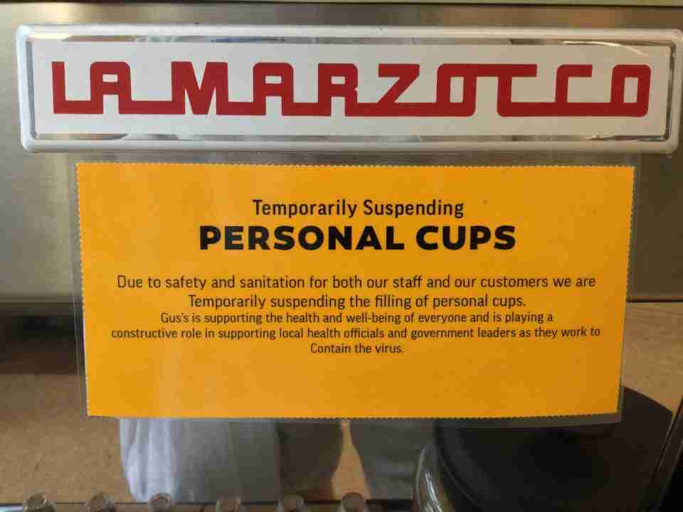 Orange printed sign stating Temporarily Suspending Personal Cups on the front of an espresso machine.