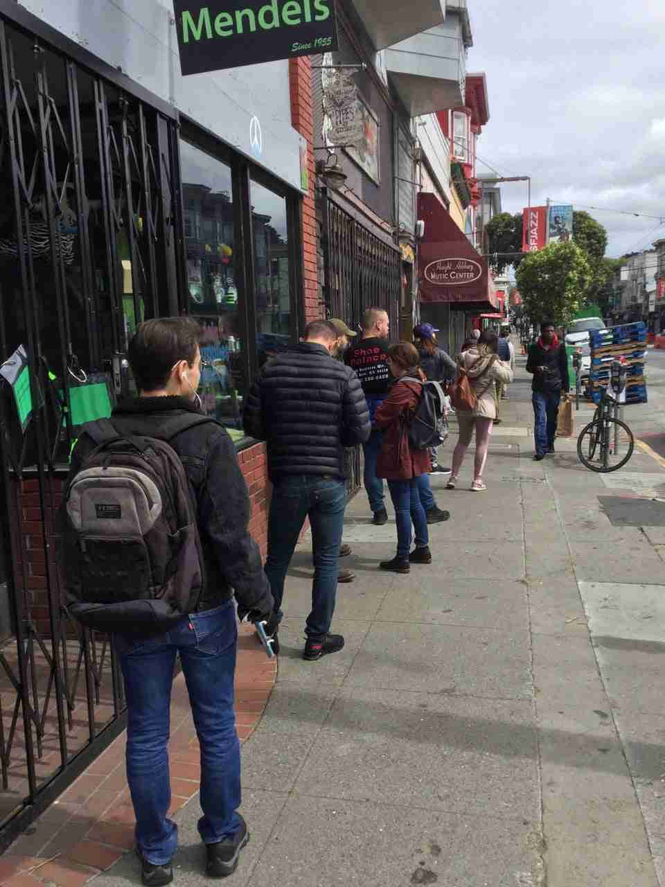 Line of people on the sidewalk on Haight Street, approximately six feet apart from each other, waiting to get into Haight Street Market.