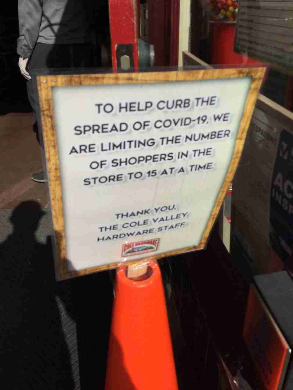 Sign in front of a store entrance with text TO HELP CURBE THE SPREAD OF COVID-19, WE ARE LIMITING THE NUMBER OF SHOPPERS IN THE STORE TO 15 AT A TIME. THANK YOU, THE COLE VALLEY HARDWARE STAFF.