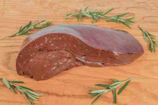 A fresh pig liver is cut on a wooden cutting board
