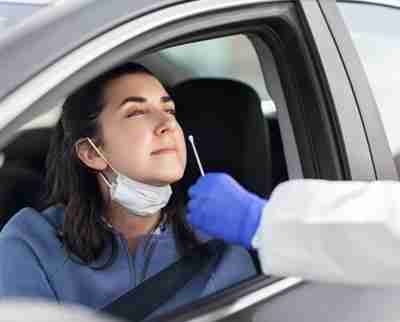 Healthcare worker in protective gear with swab taking a coronavirus test for young woman in her car
